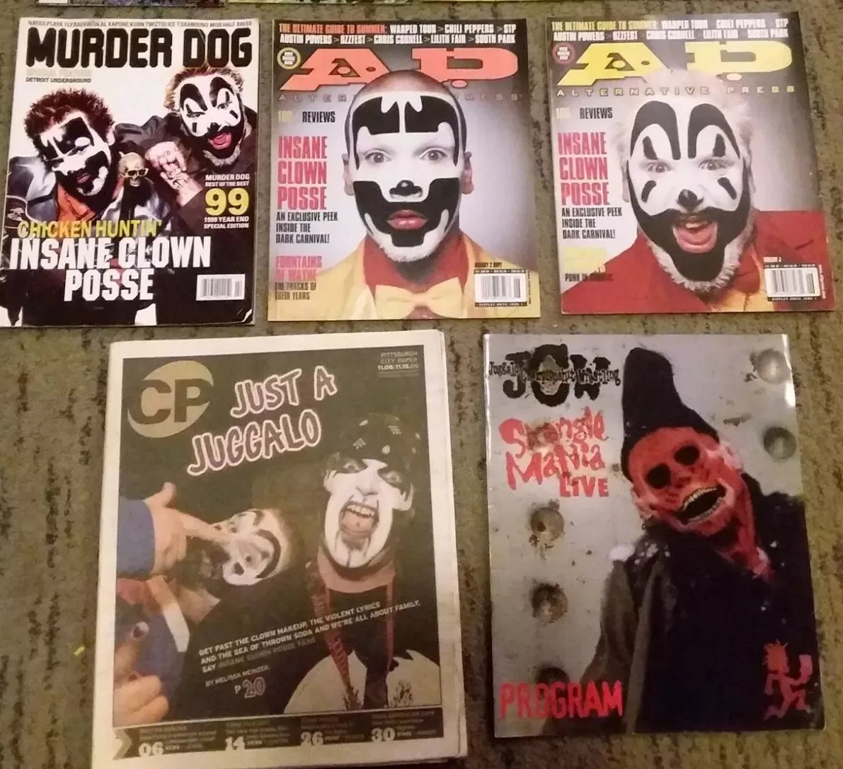 a collection of juggalo magazines organized on a table. the first one says MURDER DOG, the next two magazines are AP. at the bottom are JUST A JUGGALO and Strange Mania LIVE PROGRAM..webp