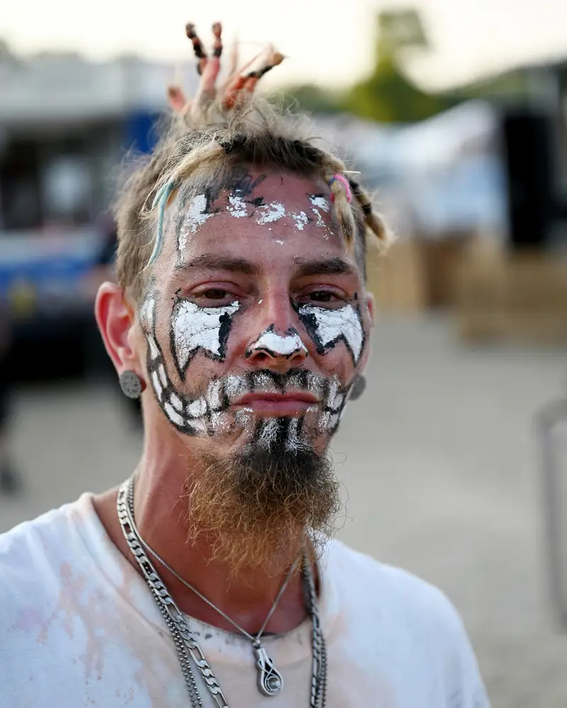 a man in poorly-done juggalo makeup that is crusted and flaking off of his face. the background is bokeh and blurry..webp