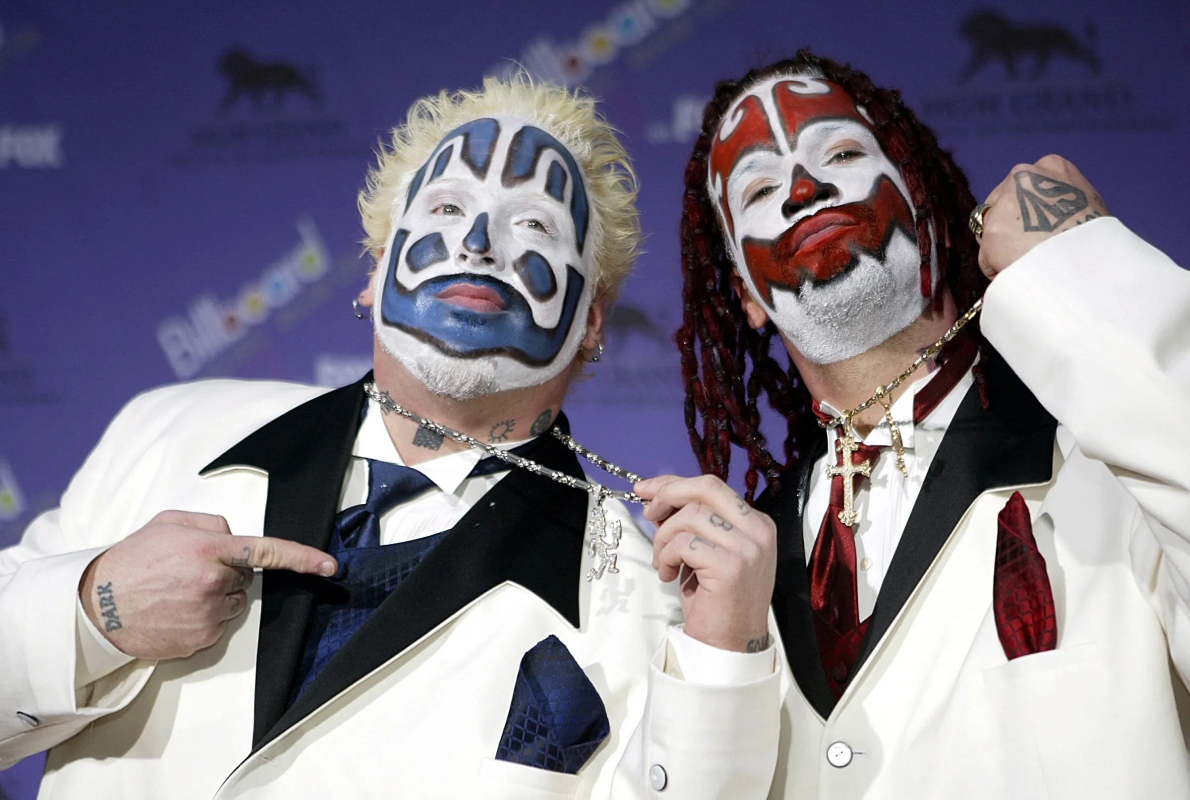 two juggalos in white suits with black accents. the left one has blue and white face paint, blonde hair. the right one has black dreads and red paint..webp